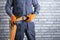 Electrician in uniform puts on a safety belt near brick wall.