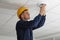 Electrician in uniform repairing ceiling lamp indoors