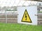 Electricity caution sign on trellised fence, on blurred city background, danger sign