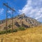 Electricity posts on grass beside a rocky mountain