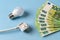 Electricity price spike. White electrical plug, light bulb and 100 euro banknotes in a fan shape over blue background. Rising of
