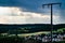 An electricity pylon in front of a cloudy sky flooded with sun rays