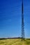 Electricity pylon seen from the side in a yellow field and steel-blue sky