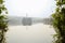 Electricity pylon on woody island in lake on foggy winter day