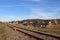 An electrified railway track among green meadows and wheat fields. Building a bridge in a small town.