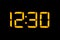 Electronic digital clock with yellow numbers on a black background shows the time Twelve thirty o`clock of the day. Isolate, clos