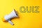 Electronic megaphone and word QUIZ on yellow background, top view