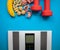 Electronic scale, banana, nuts, measuring tape and red dumbbells on a blue background