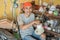 Electronics repairman smiles at the camera while holding a broken blender against the backdrop of a shelf of broken