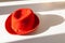 Elegance red porkpie hat decorated with a red silk band with a bow. The stylish hat is on the the white surface with hard shadow