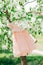 Elegance stylish peach-colored baby dress hangs on a blossoming apple tree. Green background. Spring time. Blooming apple orchard