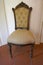 Elegant antique upholstered chair with carvings, in front of white wall.
