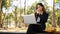 An elegant Asian businesswoman working remotely at a park, sipping coffee and working on her laptop