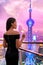 Elegant asian woman in gown drinking white wine glass at rooftop bar terrace looking at city lights skyline view of