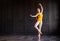 Elegant ballerina in pointe shoes in yellow leotard dancing in dark gray interior