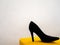 Elegant black heels on a yellow pouf chair on a white background