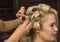 Elegant blonde woman in beauty saloon. Hairdresser does coiffure in the form of big curl. Concept wedding hairstyle