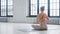 Elegant blonde yoga practitioner with hair bun in tracksuit does reverse namaste on floor near window in studio