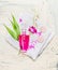 Elegant bottle of lotion , pink orchid flowers and green bamboo leaves on white towel on light wooden background, top view.