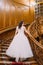 Elegant bride in white dress with long tail at old vintage palace walking up big wooden stairs