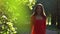 Elegant brunette girl in red dress walking along sunny park alley. Slow motion video, 120 fps