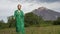 Elegant Caucasian female model in green leather coat walking in forest against background of volcano