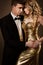 Elegant Couple, Beautiful Fashion Woman in Gold dress and Man in Tuxedo Suit, face to face