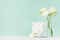 Elegant delicate celebration background with spring white flowers and closed standing square gift box on green mint menthe.