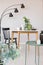 Elegant dining room with round table with vases and flowers next to black wooden chair and industrial metal lamp, real photo with