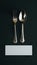 Elegant dining set with silver utensils on dark surface, white card beneath