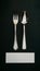 Elegant dining set with silver utensils on dark surface, white card beneath