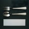 Elegant dining set with silver utensils on dark surface, white card beneath