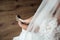 Elegant Female puts hands on wedding shoes on a background white dress, Wedding morning preparation in home