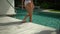 Elegant female walks into blue water swimming pool, a wears white swimwear