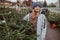 Elegant girl buys a Christmas tree. Womanin a blue cap and scarf. Beautiful lady with blond hair.