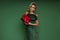 Elegant glamour blonde woman in evening feather green dress is holding red Christmas gift on green background in studio