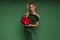 Elegant glamour blonde woman in evening feather green dress is holding red Christmas gift on green background in studio
