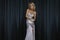 Elegant Glamour Woman is wearing sequin silver evening dress and is posing on dark velvet background