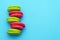 Elegant green and pink macaroons are stacked in a single line to the left on a blue background. copy space