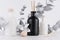 Elegant home decor with glass white, black diffuser bottles, silver branch on white wood table, wall. Blank bottles as mock up.