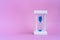 Elegant hourglass with running blue sand on pink background