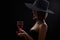 Elegant mysterious woman in a hat holding a glass of red wine on