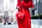 Elegant outfit. Closeup of red leather bag in hands of stylish woman. Fashionable girl on the street. Female fashion. City lifesty