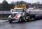 Elegant powerful big rig semi truck with step down flat bed trailer on construction side