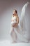 Elegant pregnant young woman standing wearing flying white fabric. Pregnancy, maternity and motherhood concept.