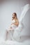 Elegant pregnant young woman standing wearing flying white fabric. Pregnancy, maternity and motherhood concept.