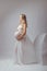 Elegant pregnant young woman standing wearing flying white fabric. Pregnancy, maternity and motherhood concept.