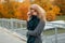 Elegant pretty young woman in stylish gray coat with checkered green scarf posing standing outdoors in autumn day.