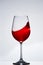 Elegant pure wineglass with wave of brightly red wine standing against light background with reflection in down.