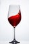 Elegant pure wineglass with wave of brightly red wine standing against light background with reflection in down.